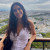 Sofia Weingarten stands outside over city view, smiling to camera 